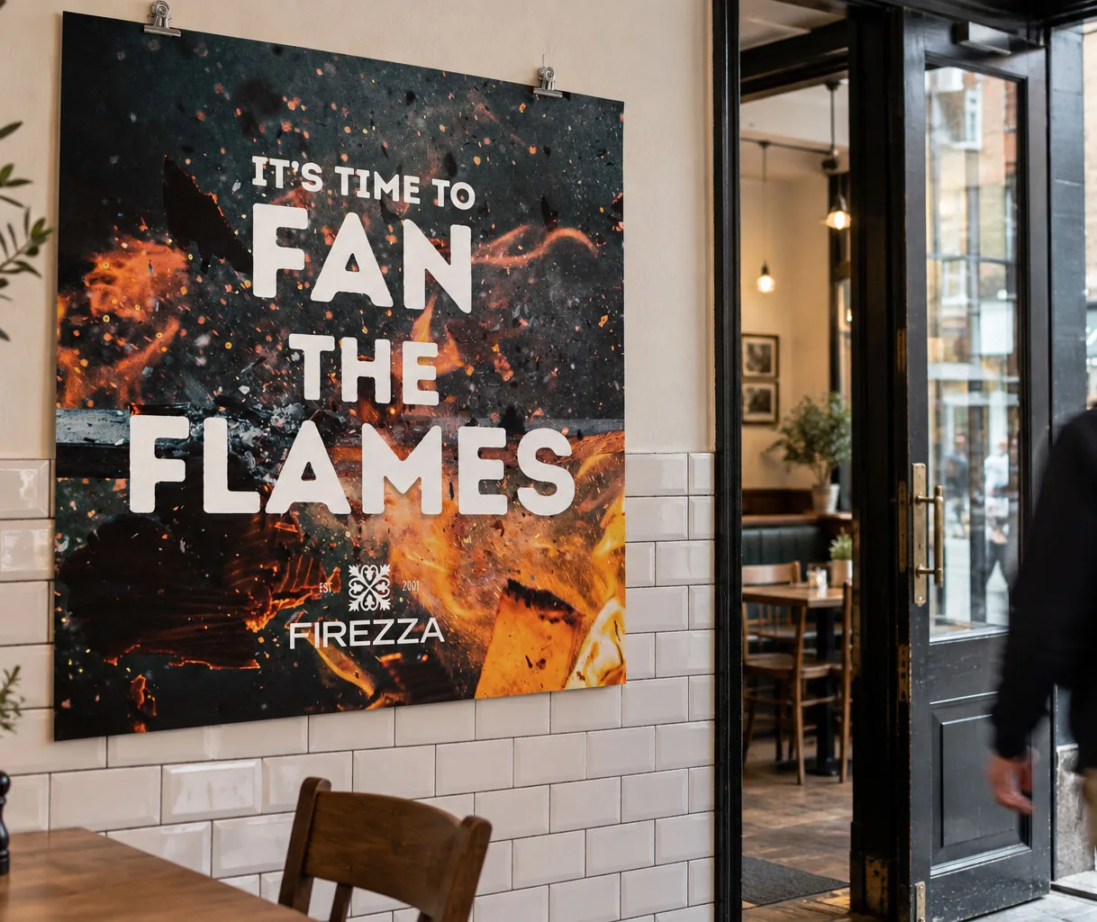 A Firezza poster reading It’s time to fan the flames, over glowing embers, on a tiled restaurant wall