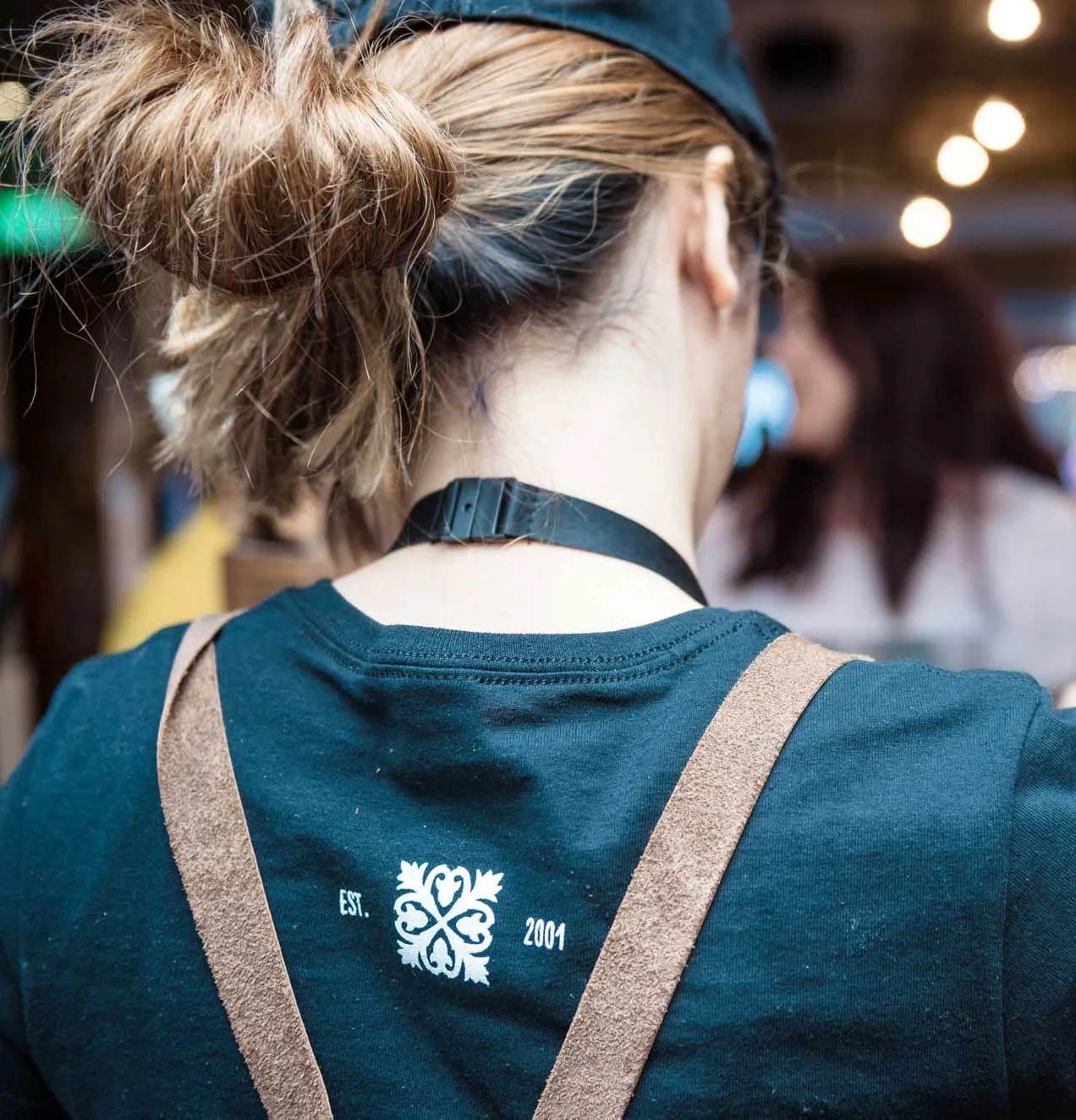 A member of staff from behind, wearing a teal Firezza T-shirt and apron with the Firezza emblem
