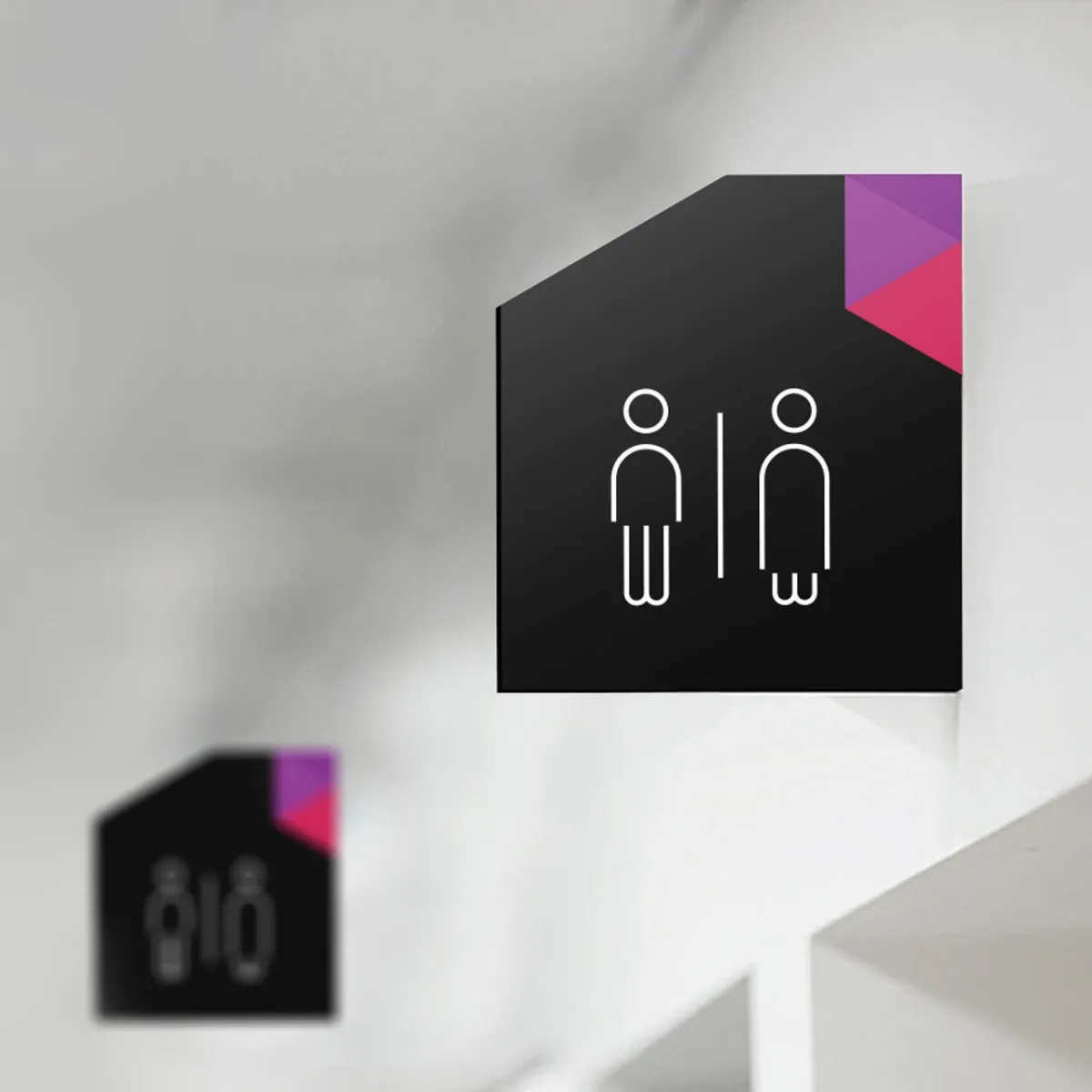 A black Plexal toilet sign with a coloured corner, mounted on a white wall