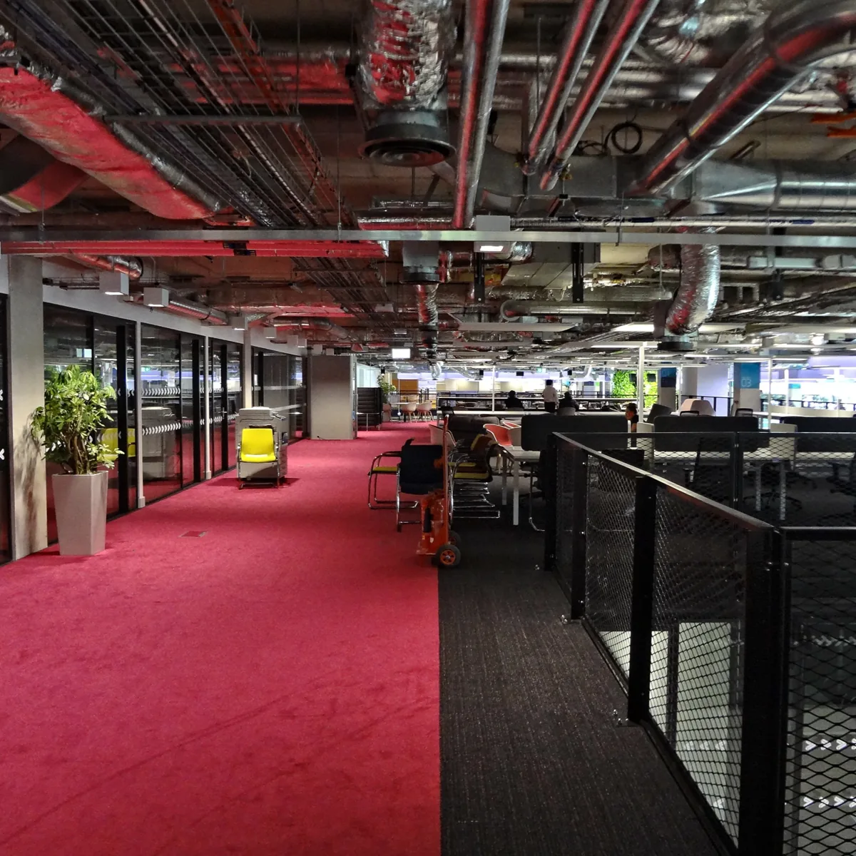 A long Plexal corridor with red carpet, exposed ceiling ducts and workspaces either side