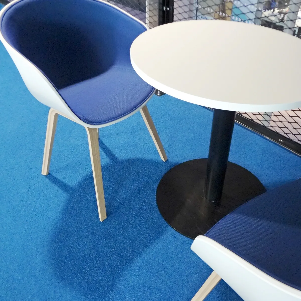 Blue chairs around a white table on bright blue carpet at Plexal