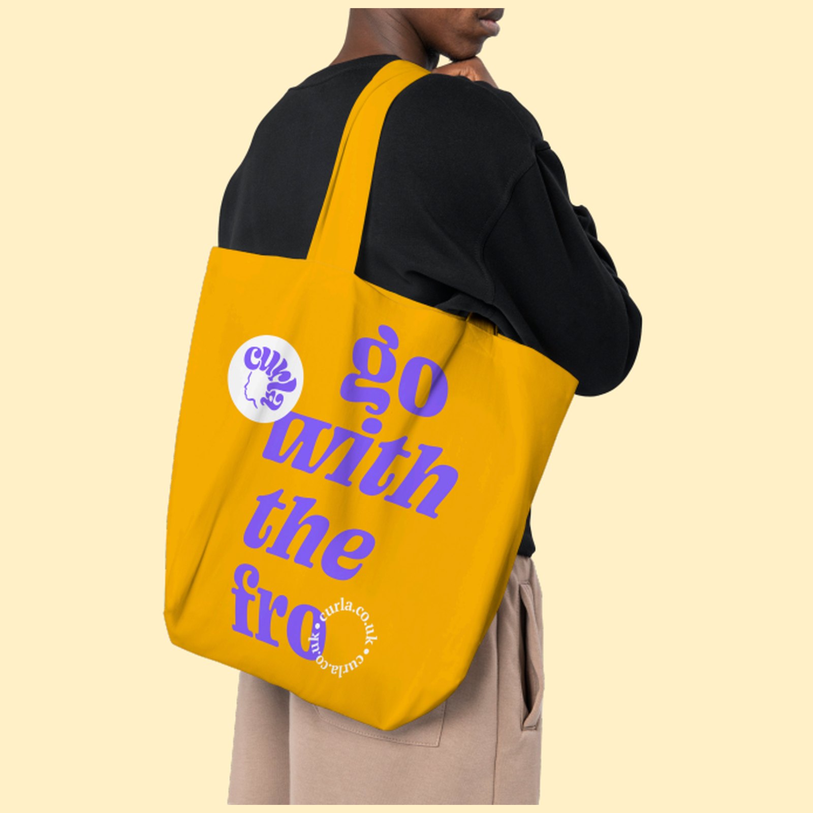 A yellow Curla tote bag carried on the shoulder, printed in violet with go with the fro and a small curla logo