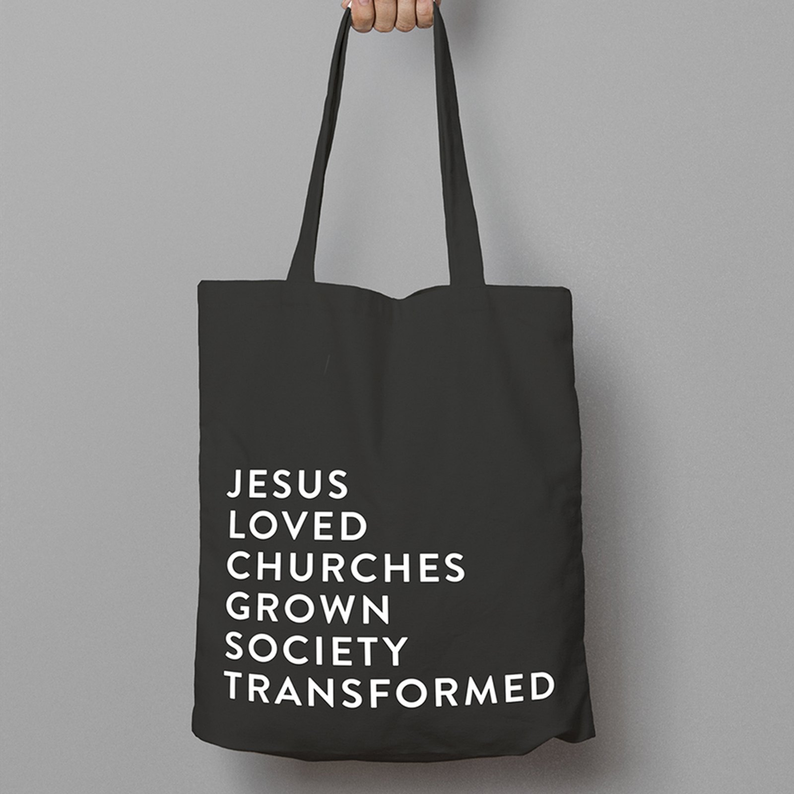 A black tote bag printed in white capitals with the church’s vision: Jesus loved, churches grown, society transformed