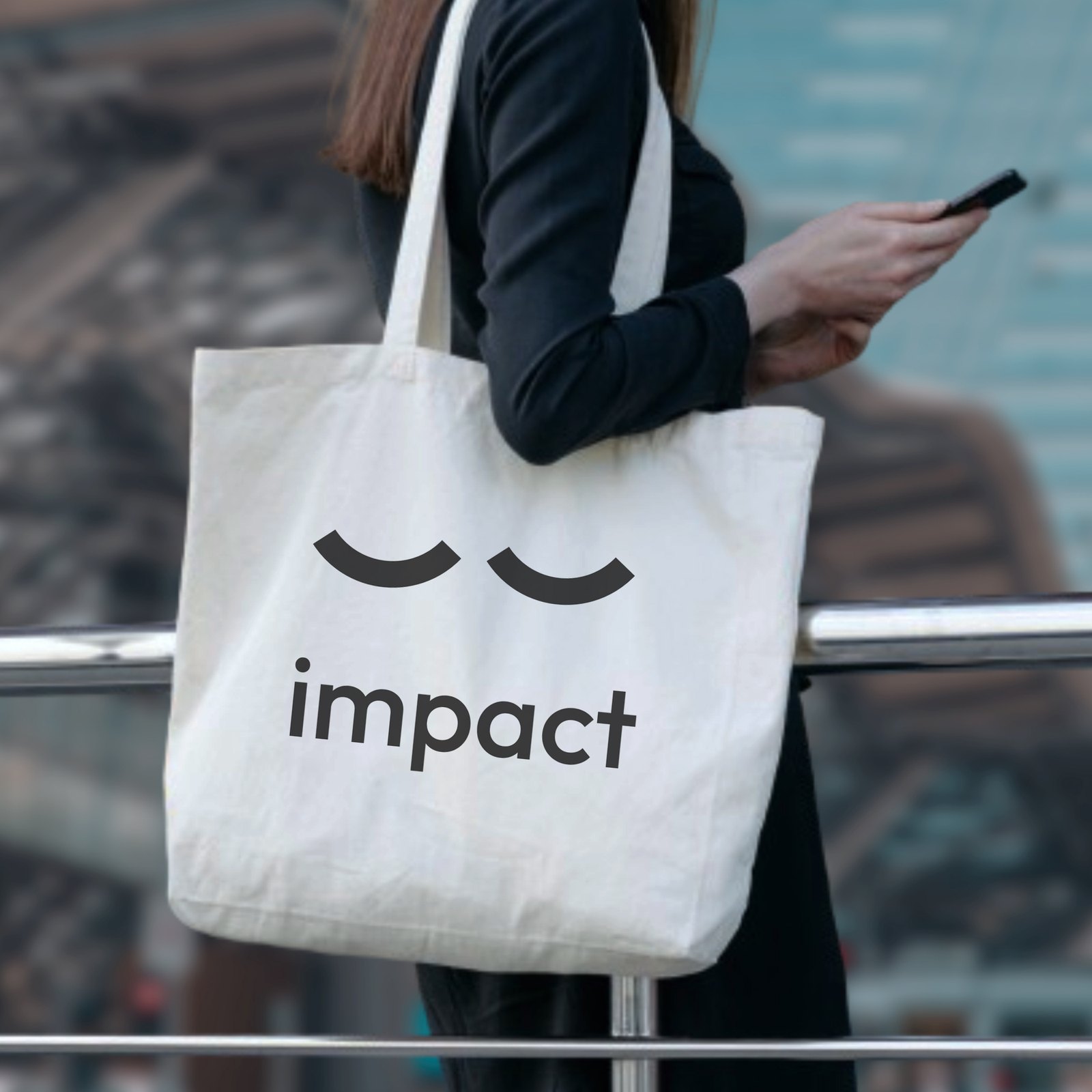 A canvas tote bag carried over the shoulder, printed with two closed eyes above the word impact in black