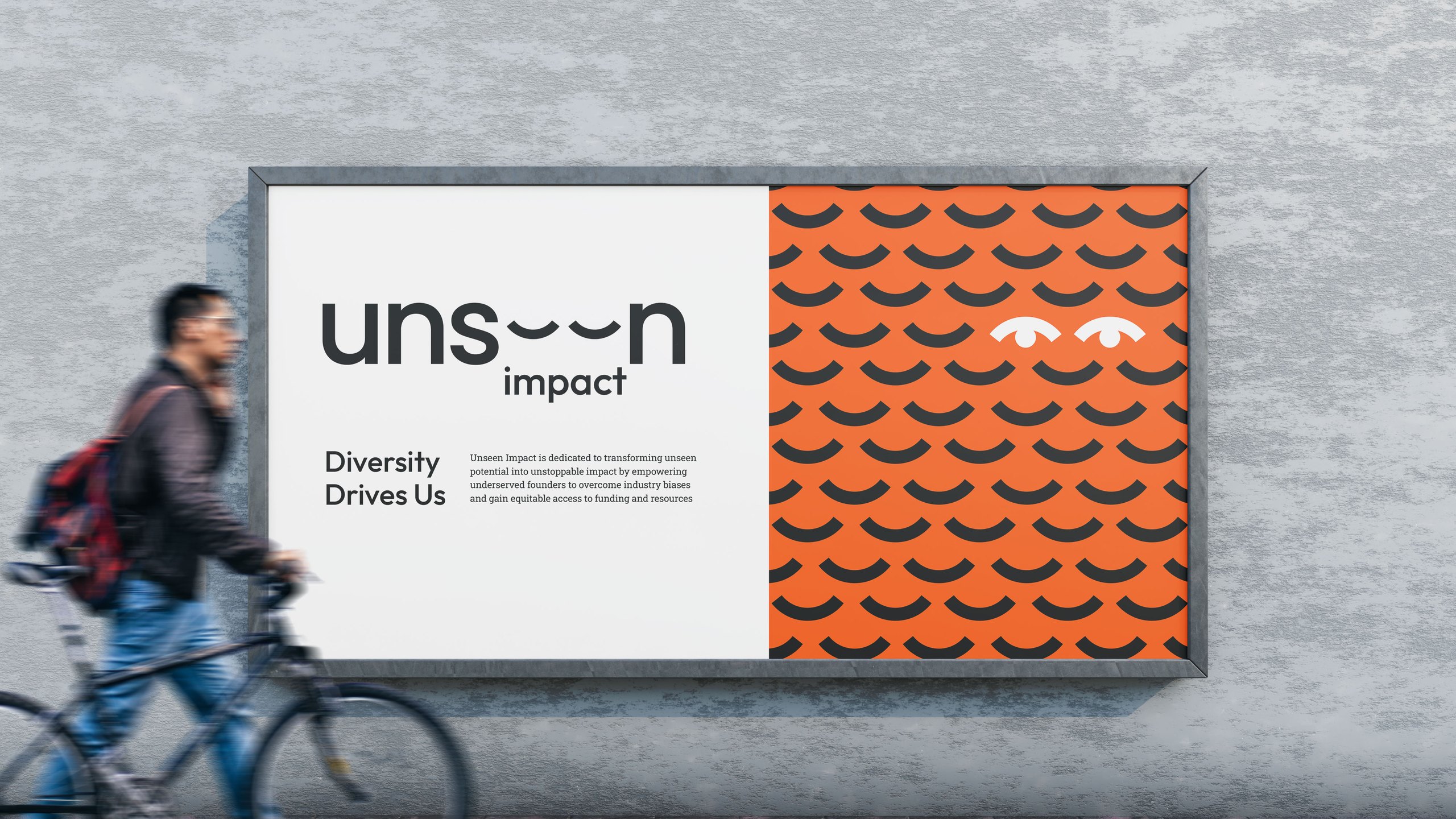 A wall billboard with the unseen impact wordmark, the line Diversity Drives Us and the mission statement beside an orange pattern of closed eyes with one pair open, as a cyclist passes