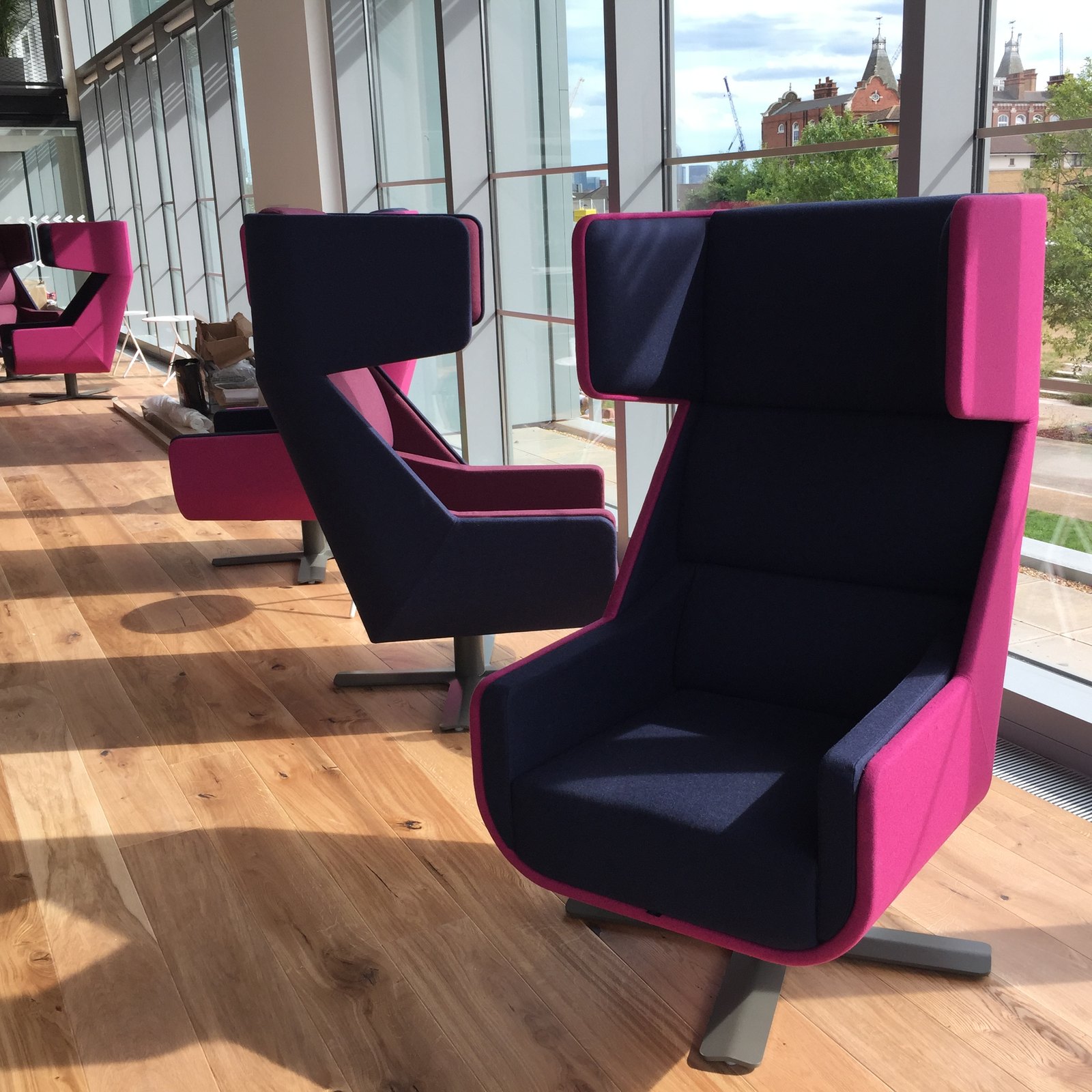 High-backed acoustic armchairs in navy and pink lined up beside the windows at Plexal