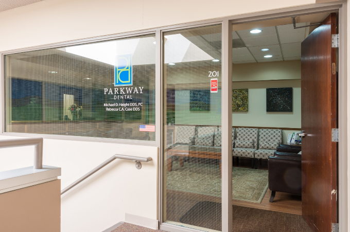 Exterior entrance of Parkway Dental showing glass door with practice logo and suite number 201