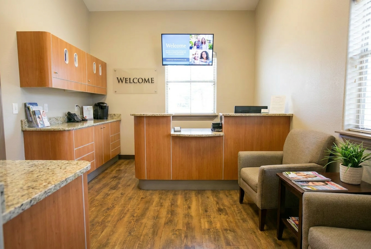 Modern dental office reception area with wood cabinetry, granite countertops, comfortable seating, and a welcoming front desk with natural lighting