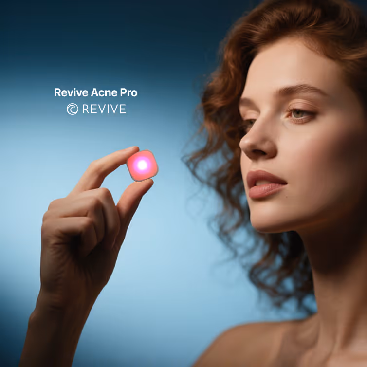 Mujer con piel clara y cabello rizado rojo sostiene un dispositivo pequeño que emite luz roja y rosa, con texto 'Revive Acne Pro' y logo de Revive al fondo azul.
