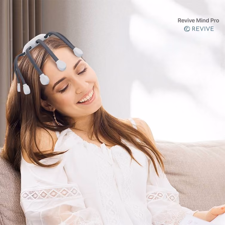 Mujer sonriente con los ojos cerrados usando un dispositivo Revive Mind Pro en la cabeza mientras está sentada en un sofá.