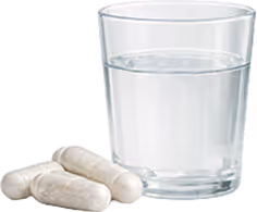 Vaso de agua junto a tres cápsulas blancas de suplemento.