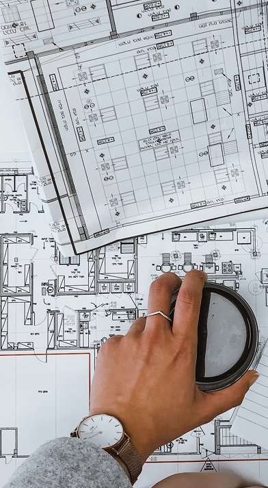 Mano sobre planos de construcción con lupa, mostrando detalles del diseño arquitectónico.