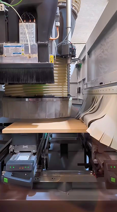 Máquina industrial con panel de madera y tubos para extracción o ventilación, en proceso de mecanizado.