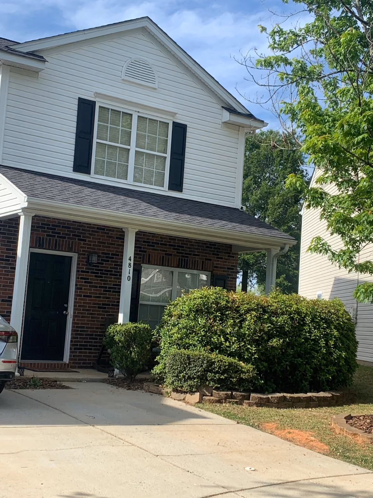 Two-story house with white siding and brick facade, black shutters, and green bushes in front yard.