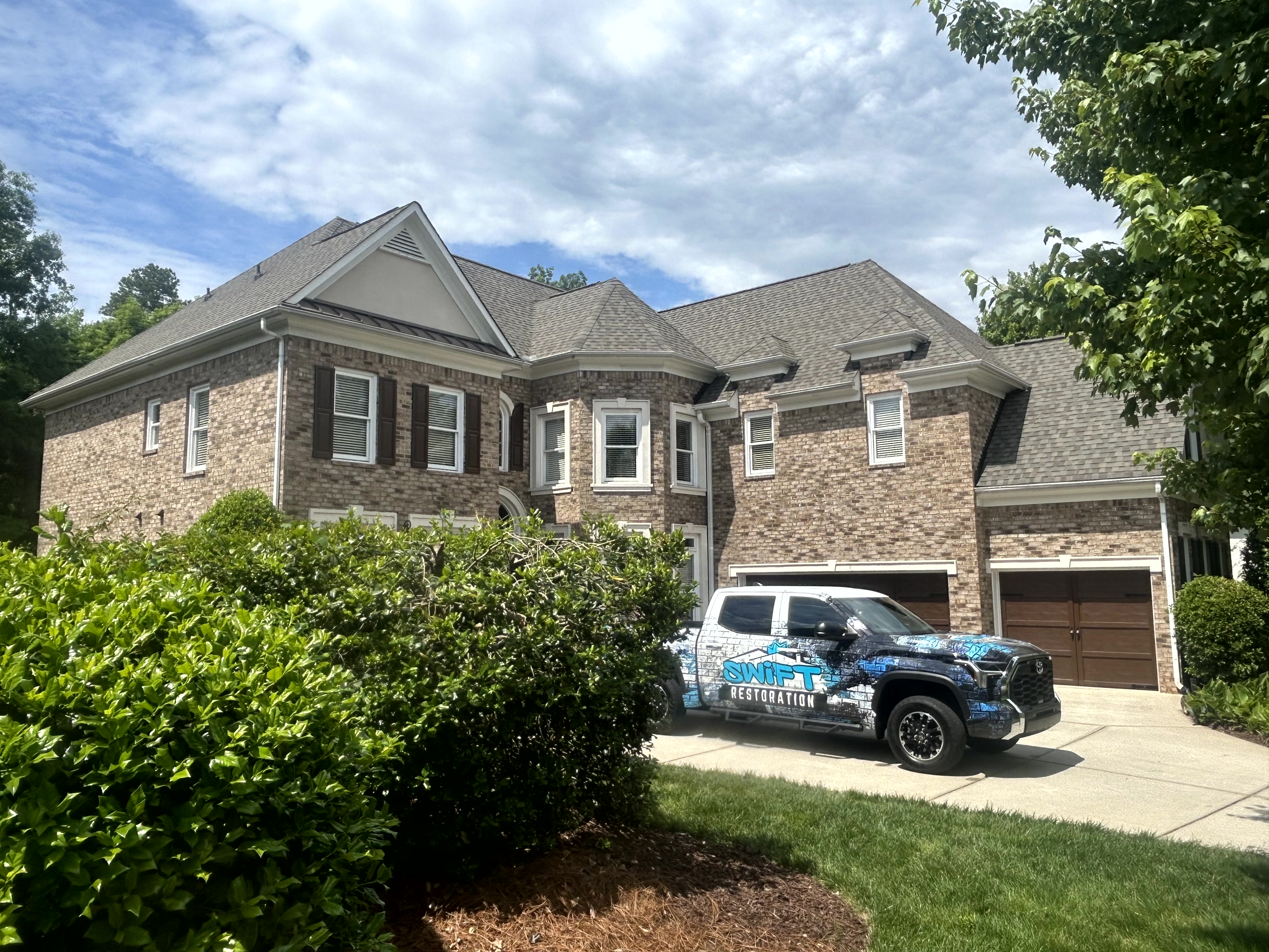 Brick two-story house with a Swift Restoration truck parked in the driveway under a partly cloudy sky.