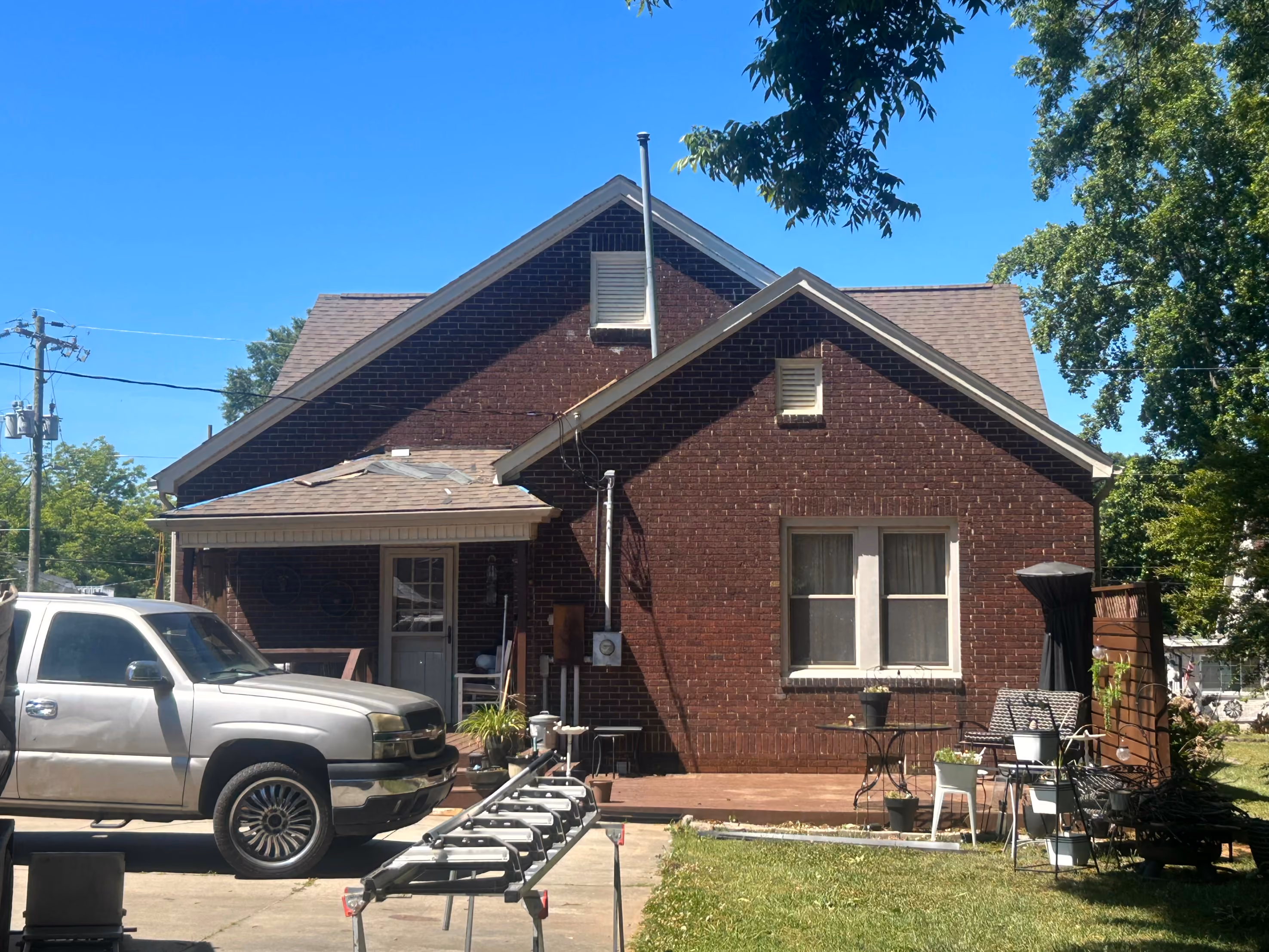 Back of a brick house with a silver pickup truck, patio furniture, and a clear blue sky.