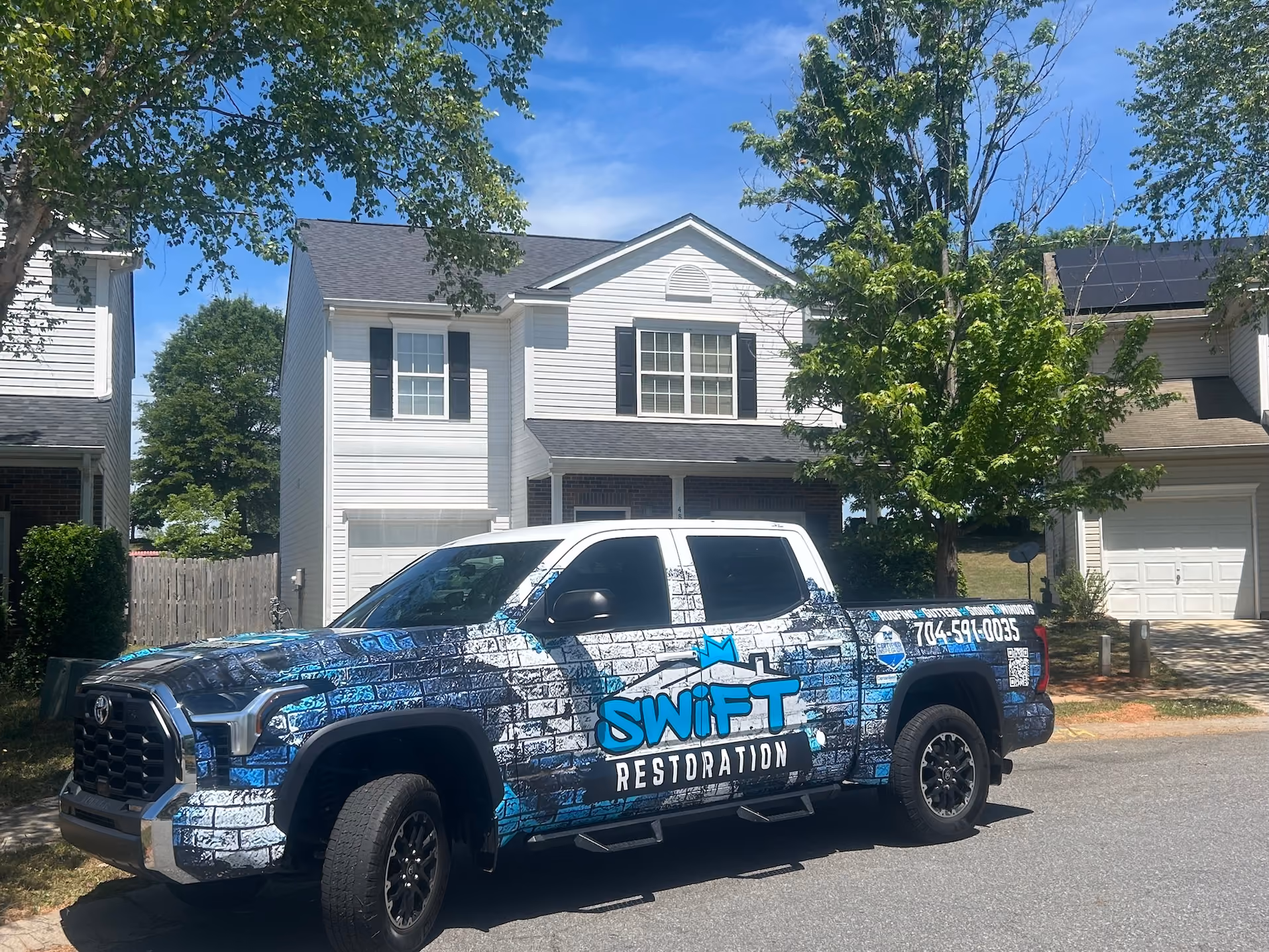 Blue and black Swift Restoration pickup truck with brick pattern parked in front of white house.