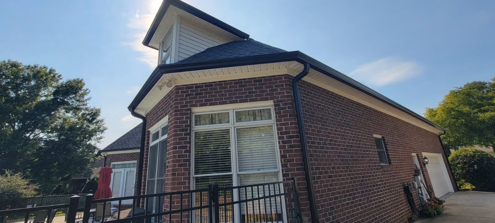 Two-story brick house with white windows, black roof gutters, and a driveway on a sunny day.