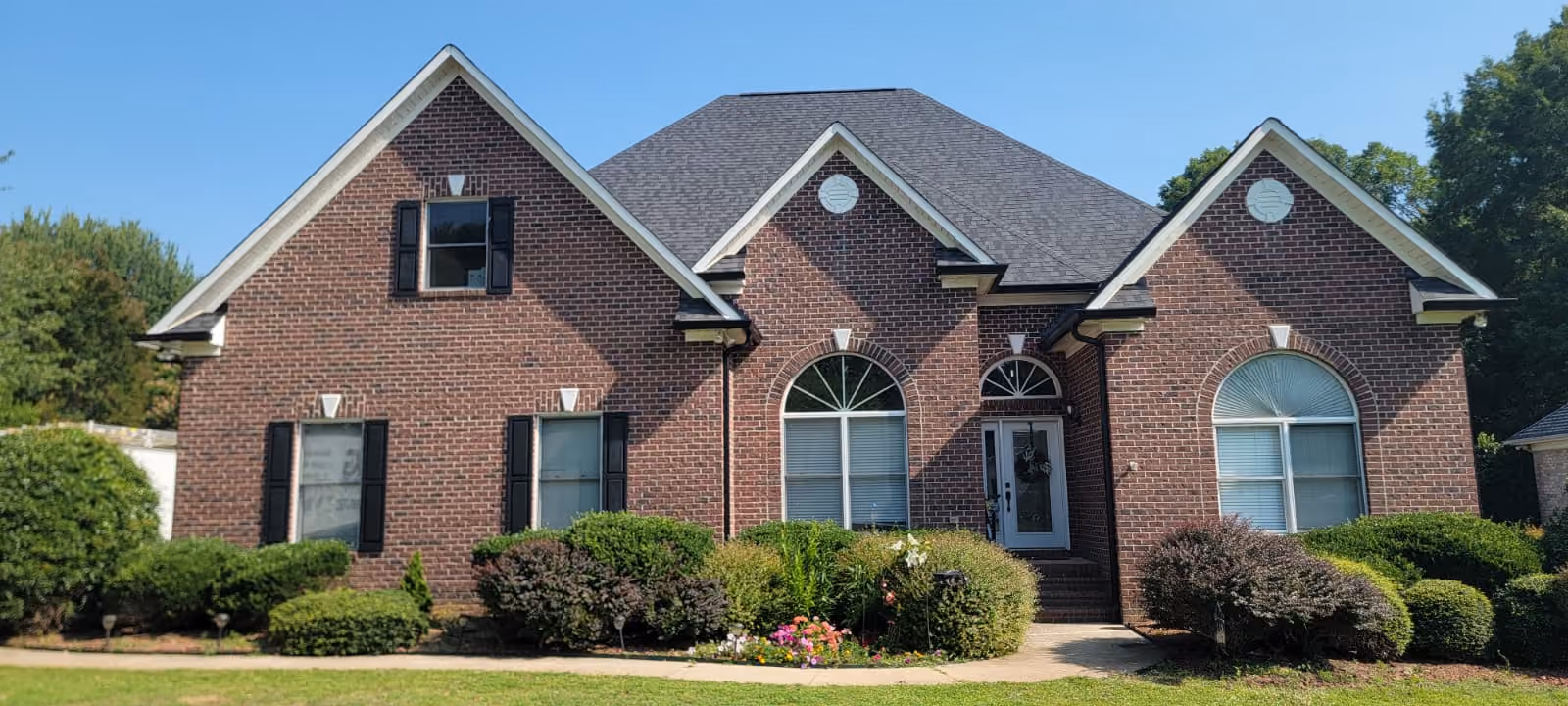 Brick house with three gable roofs, arched front windows, white door, and trimmed bushes.