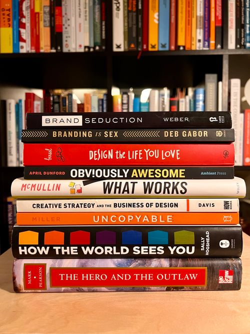 A stack of books on branding in front of a full bookshelf full of books.