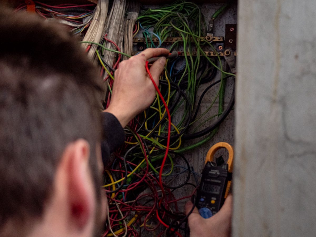 An eCertify electrician working through old cabling inside a wall box