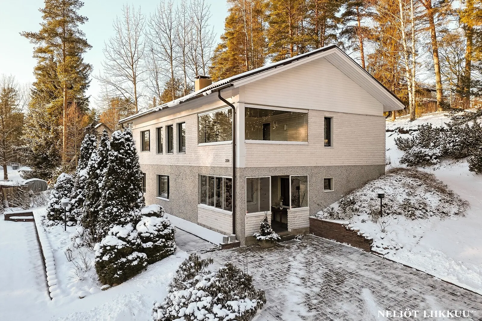 Kaksikerroksinen omakotitalo lumisessa männikkömaisemassa Lahdessa.