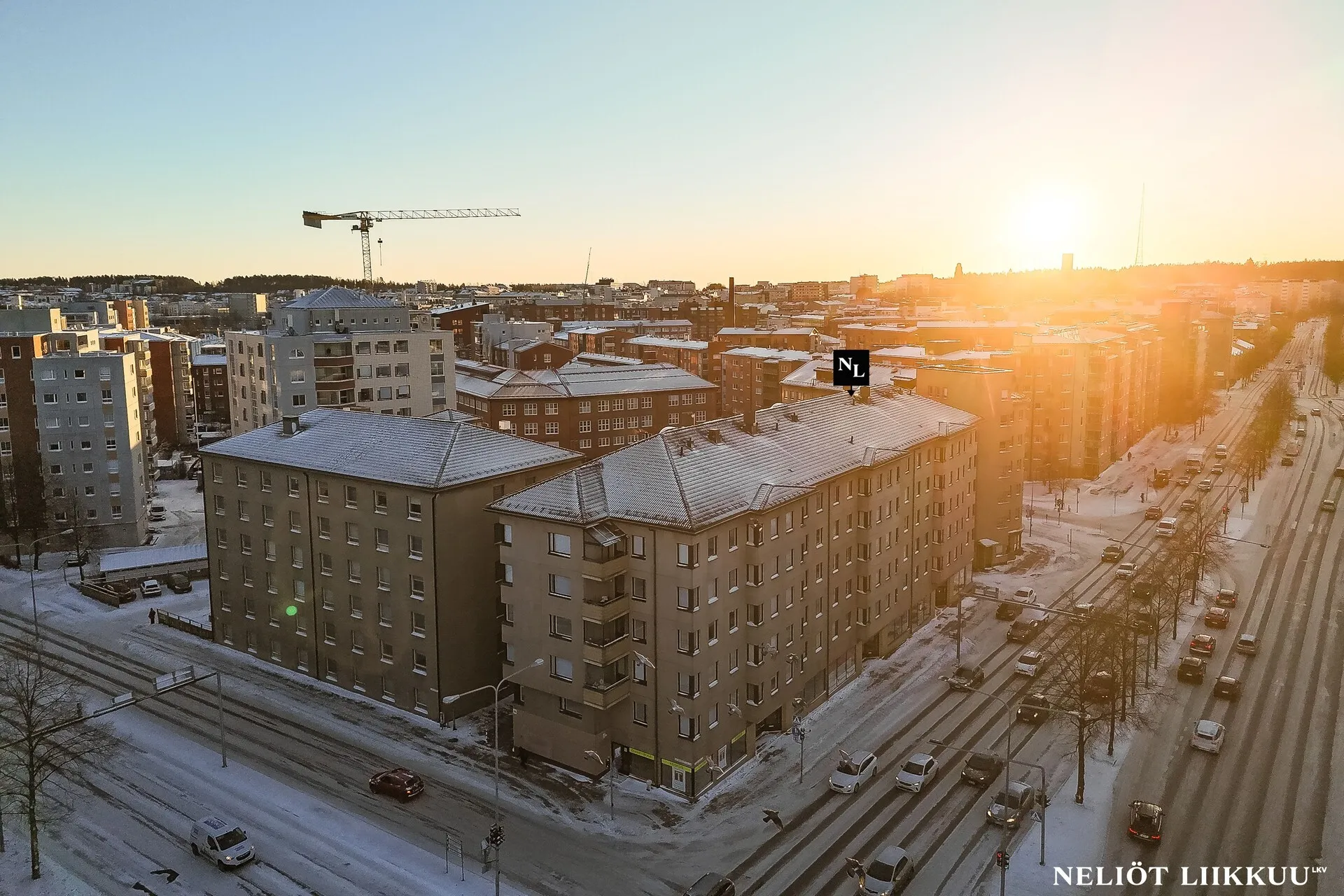 Yläilmakuva talvisesta kaupunkimaisemasta, jossa kerrostalot ja katuverkosto erottuvat auringonlaskussa.