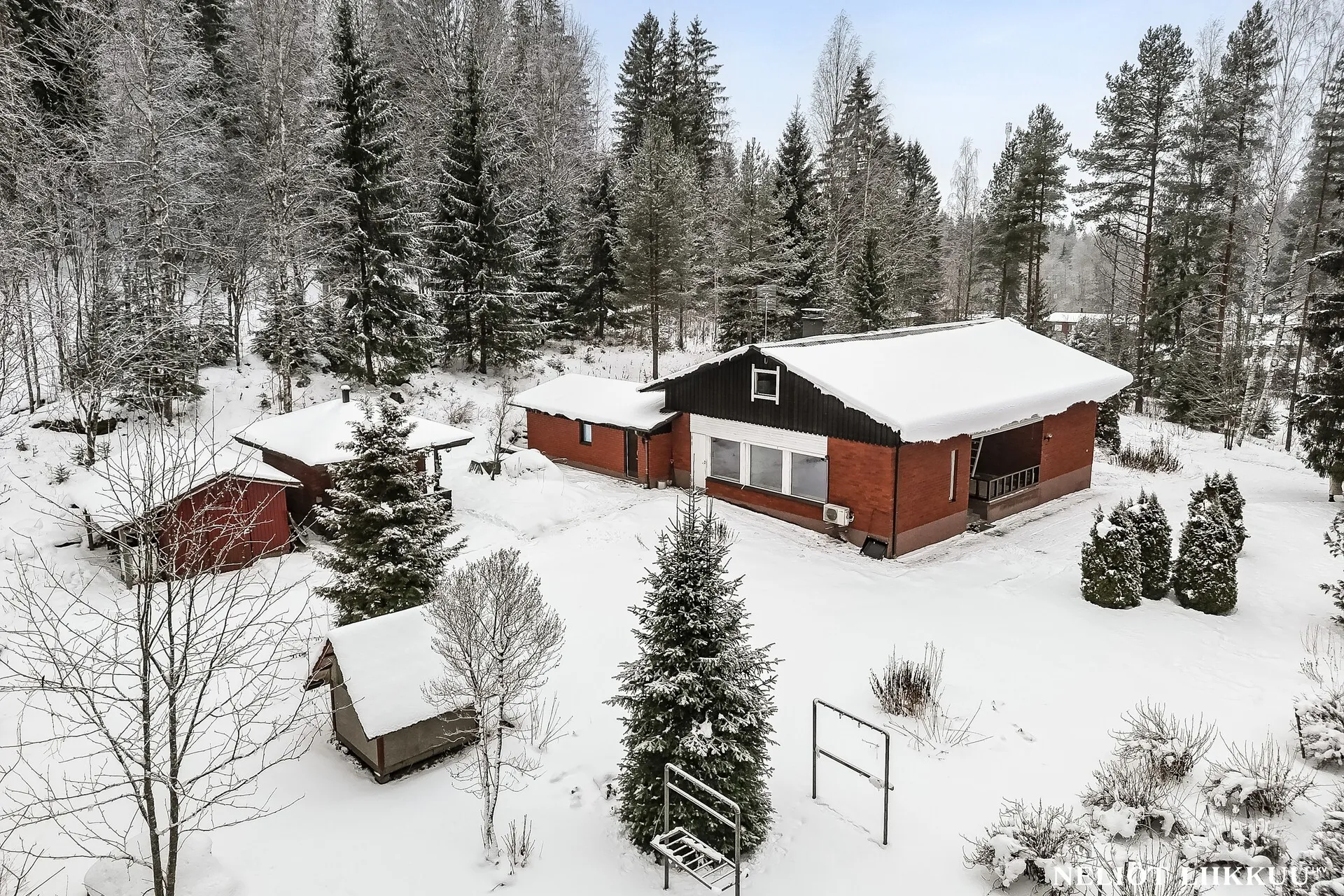 Omakotitalo ja pihapiiri lumisessa talvimaisemassa metsän reunalla.