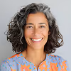 Smiling woman with curly gray hair wearing a colorful patterned top.