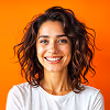 Smiling woman with curly brown hair wearing a white shirt against an orange background.