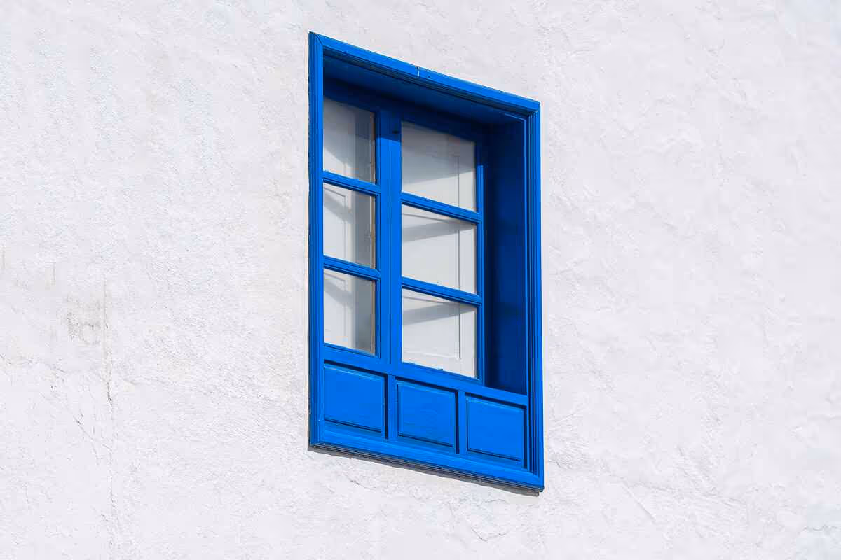 Blue wooden window frame with glass panes set in a white textured wall.