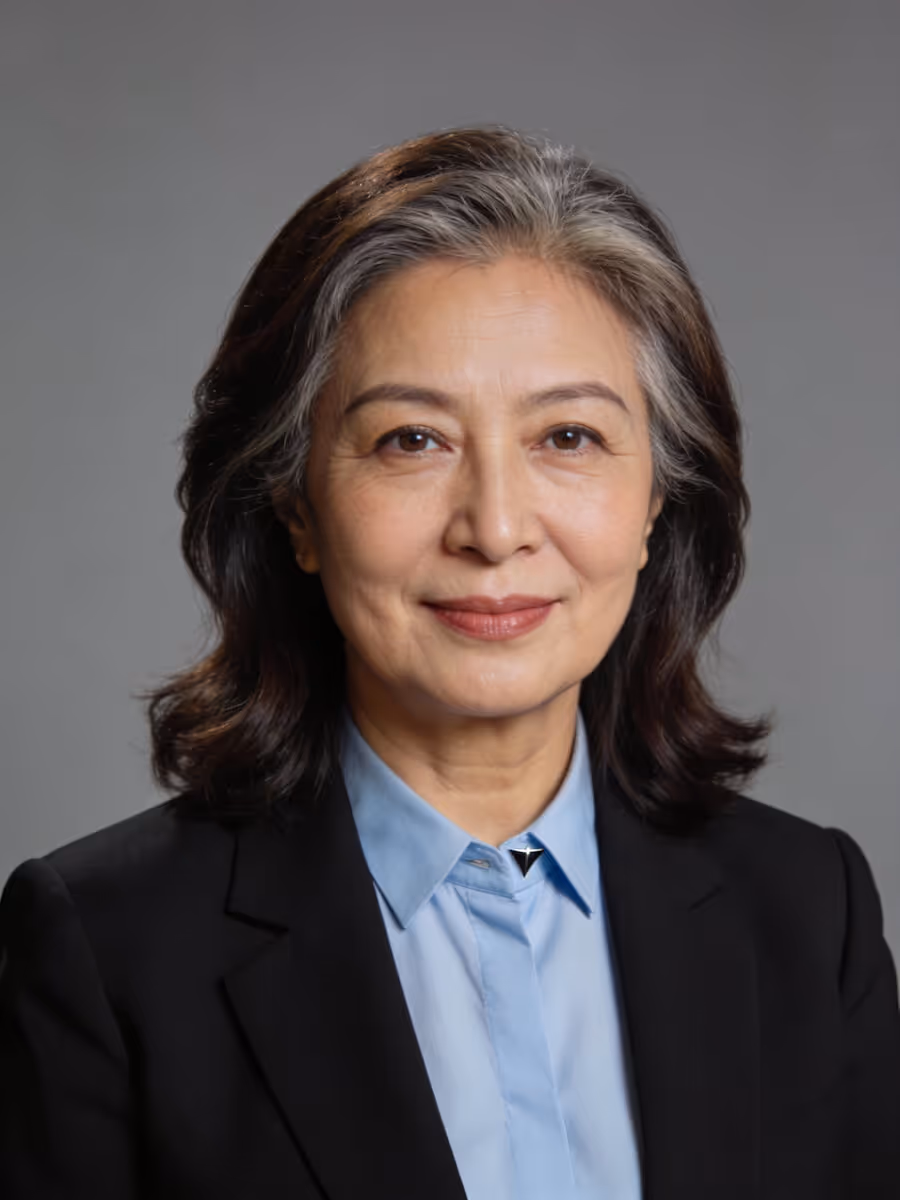 Smiling mature woman with salt-and-pepper hair in a blue shirt and black blazer against gray background.
