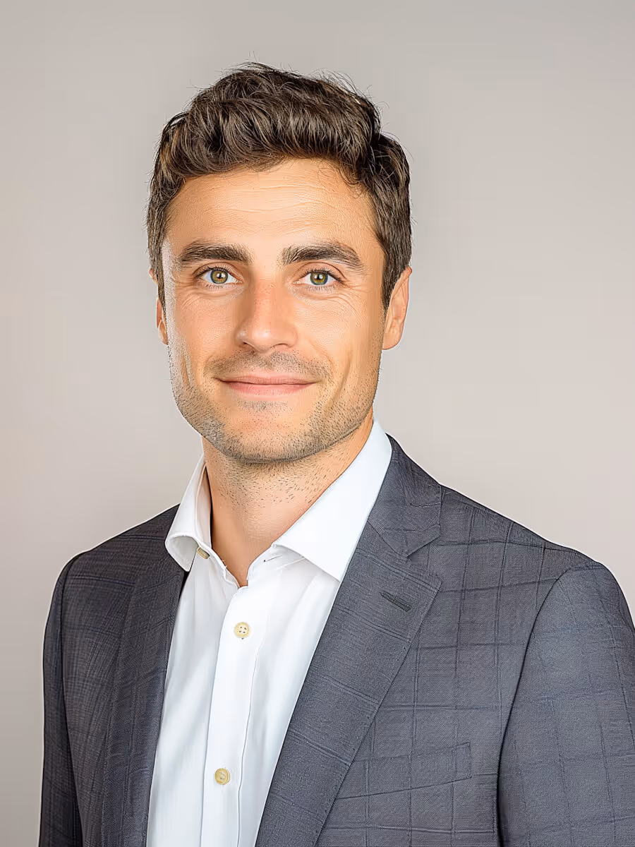 Smiling man with short brown hair wearing gray checkered suit and white shirt on neutral background.