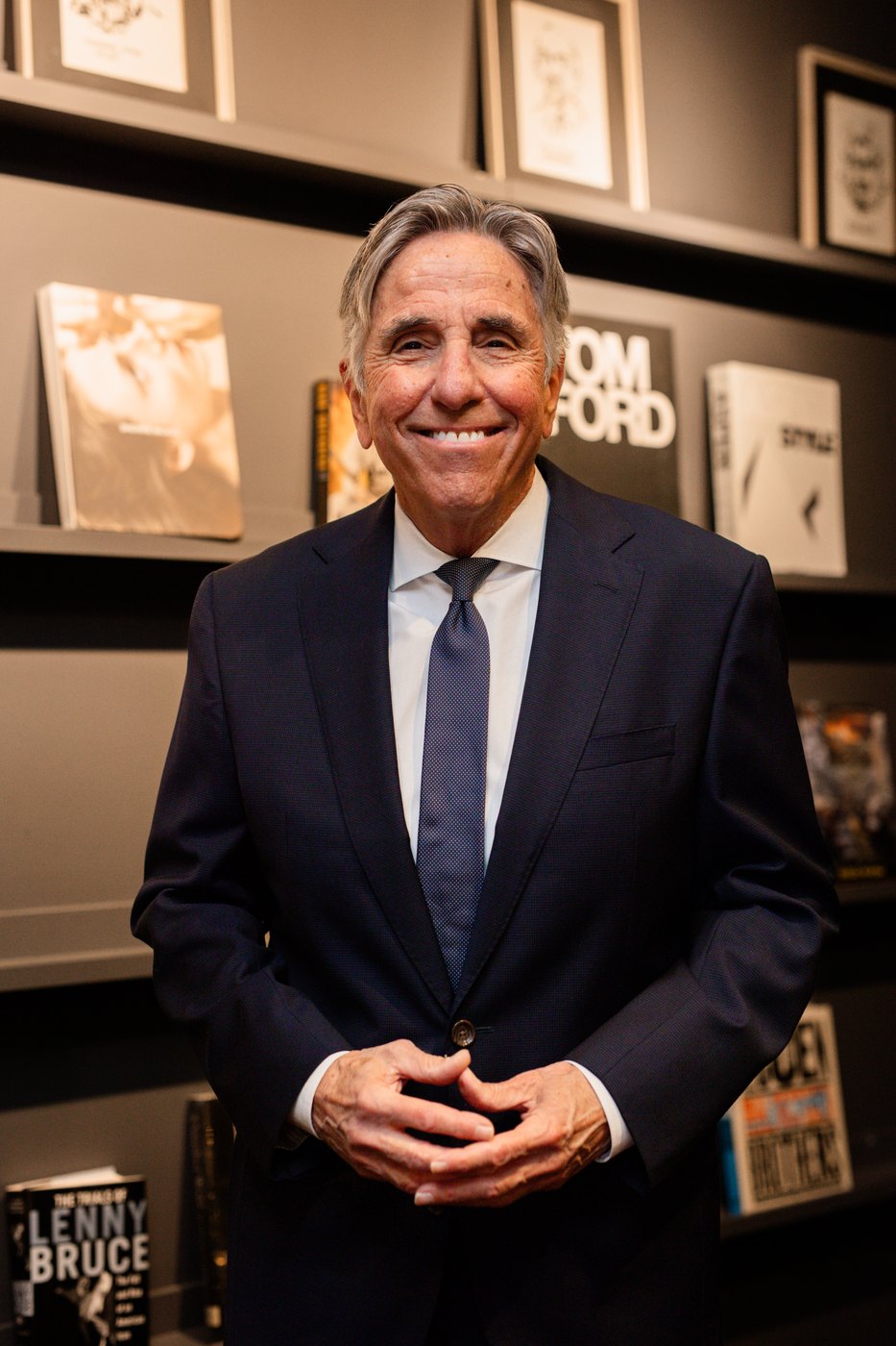 Bernie Smilovitz smiling in a navy suit and tie in front of a designer bookshelf