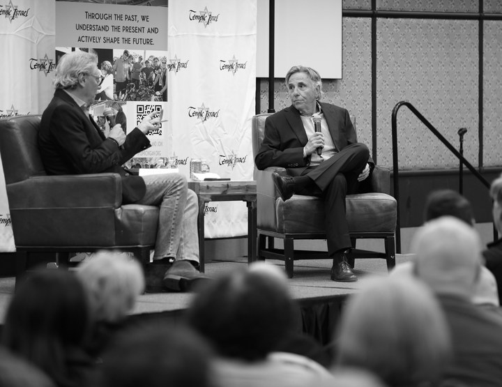 Bernie Smilovitz on stage with an interviewer at a Temple Israel Q&A in front of an audience