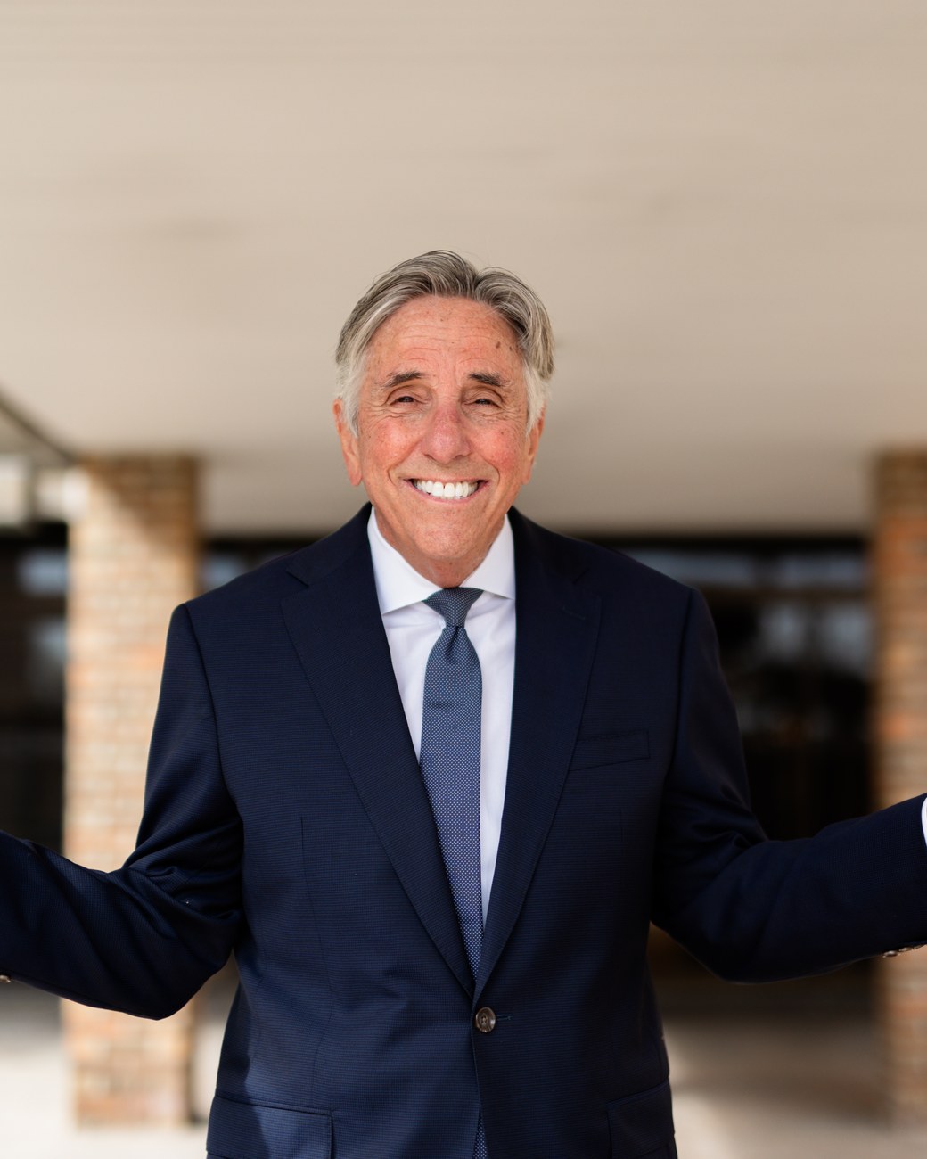 Bernie Smilovitz smiling with his arms spread wide in a welcoming gesture