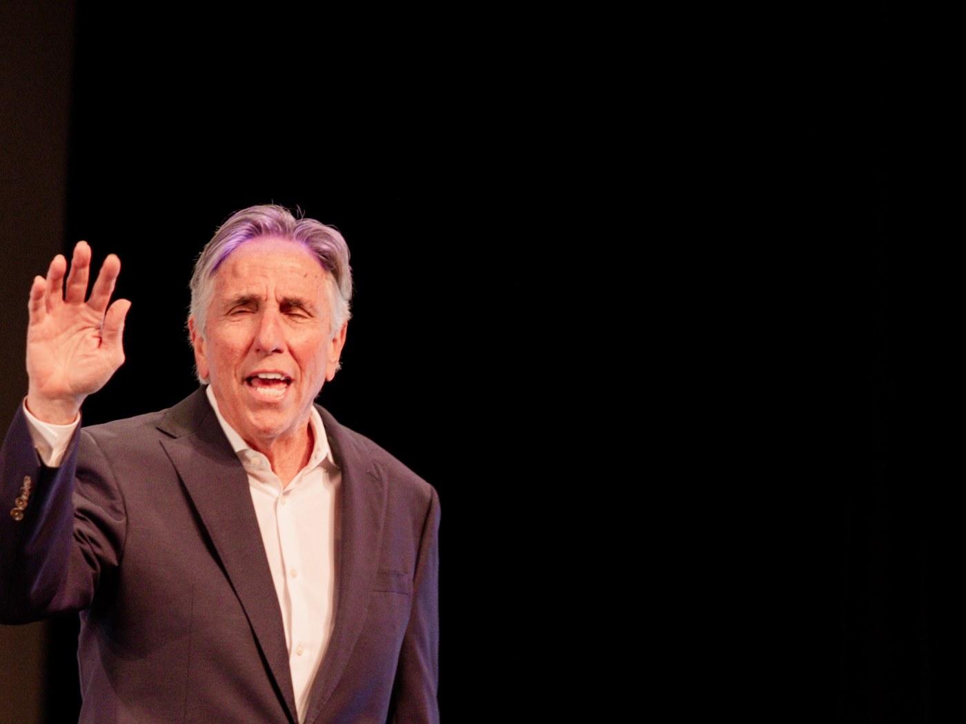 Bernie Smilovitz in a navy suit waving to the audience on a theater stage