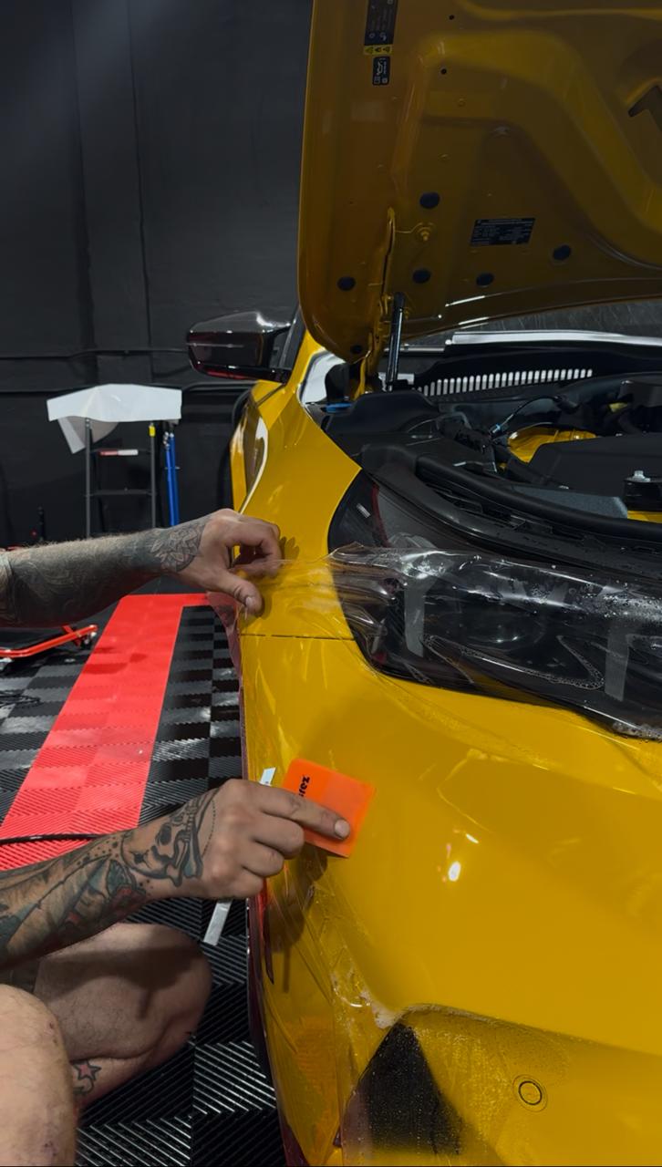 Technician wrapping protective film around a yellow supercar headlight