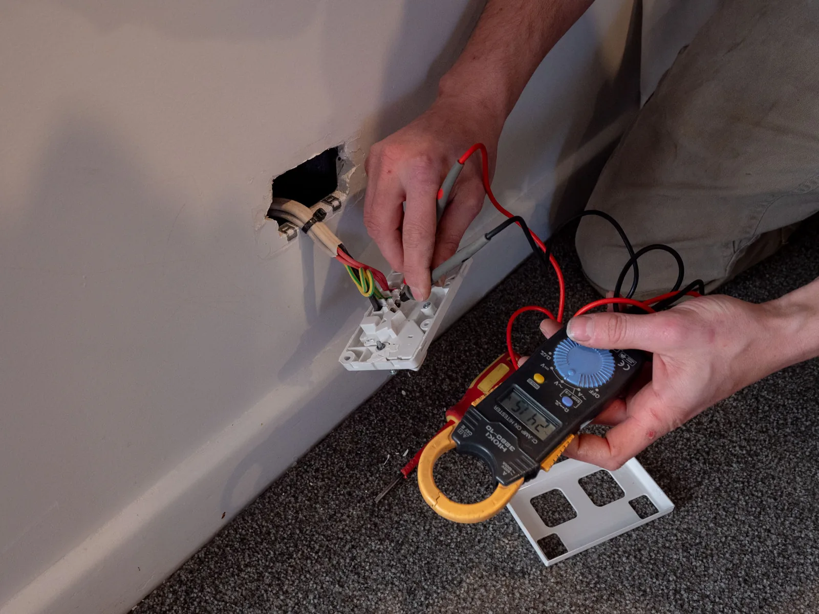 Hands testing a wiring point pulled from a wall cavity