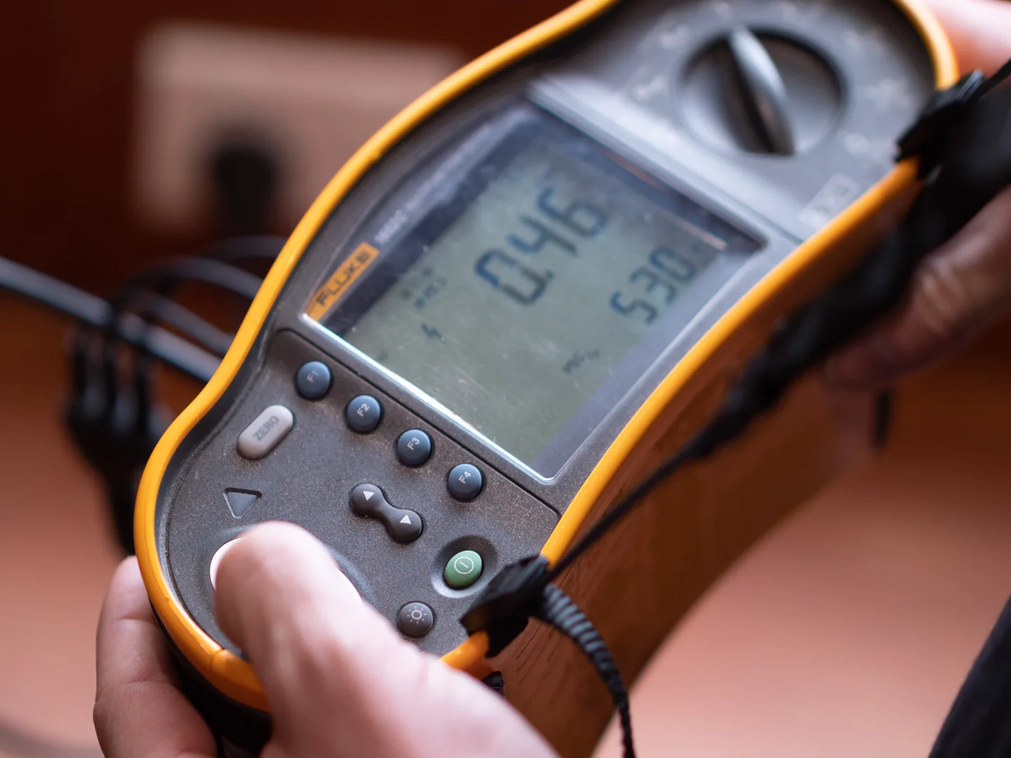 Multifunction electrical tester held in two hands, screen lit