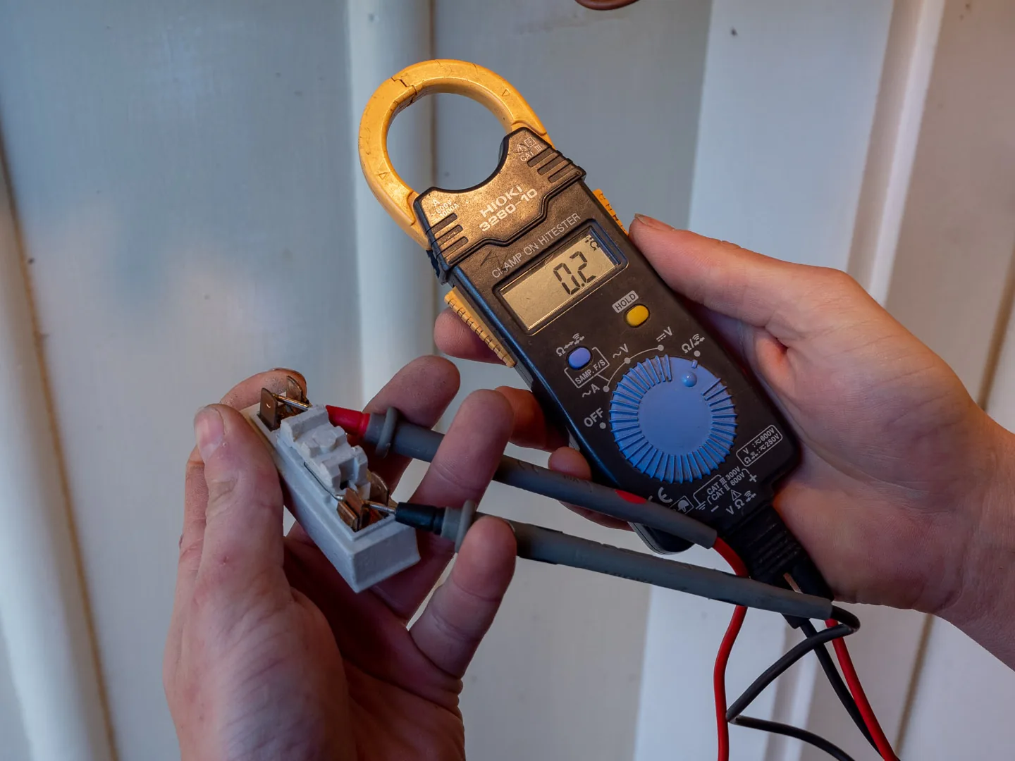 Clamp meter testing a ceramic fuse carrier pulled from a switchboard