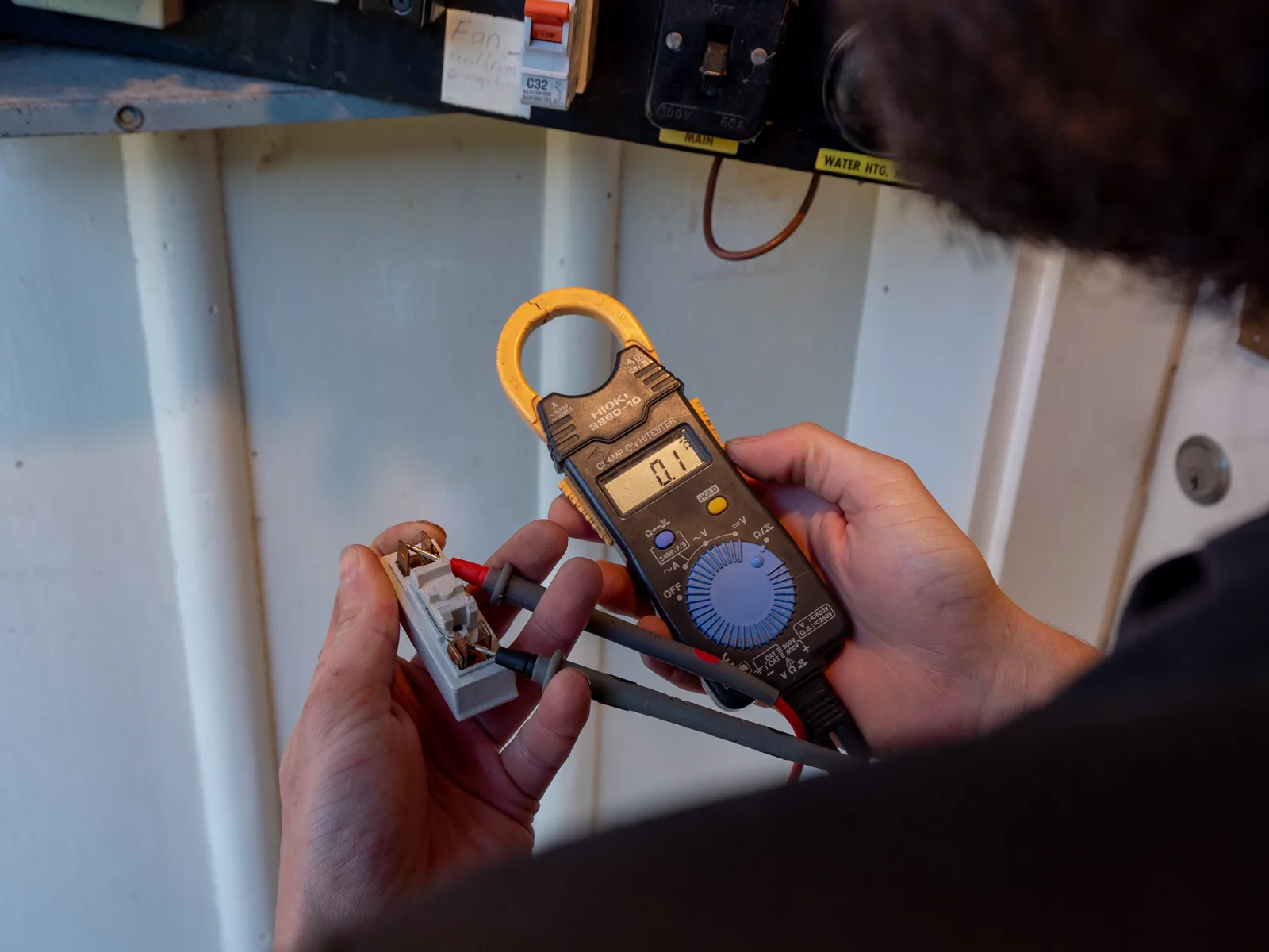 Clamp meter testing a ceramic fuse carrier by hand