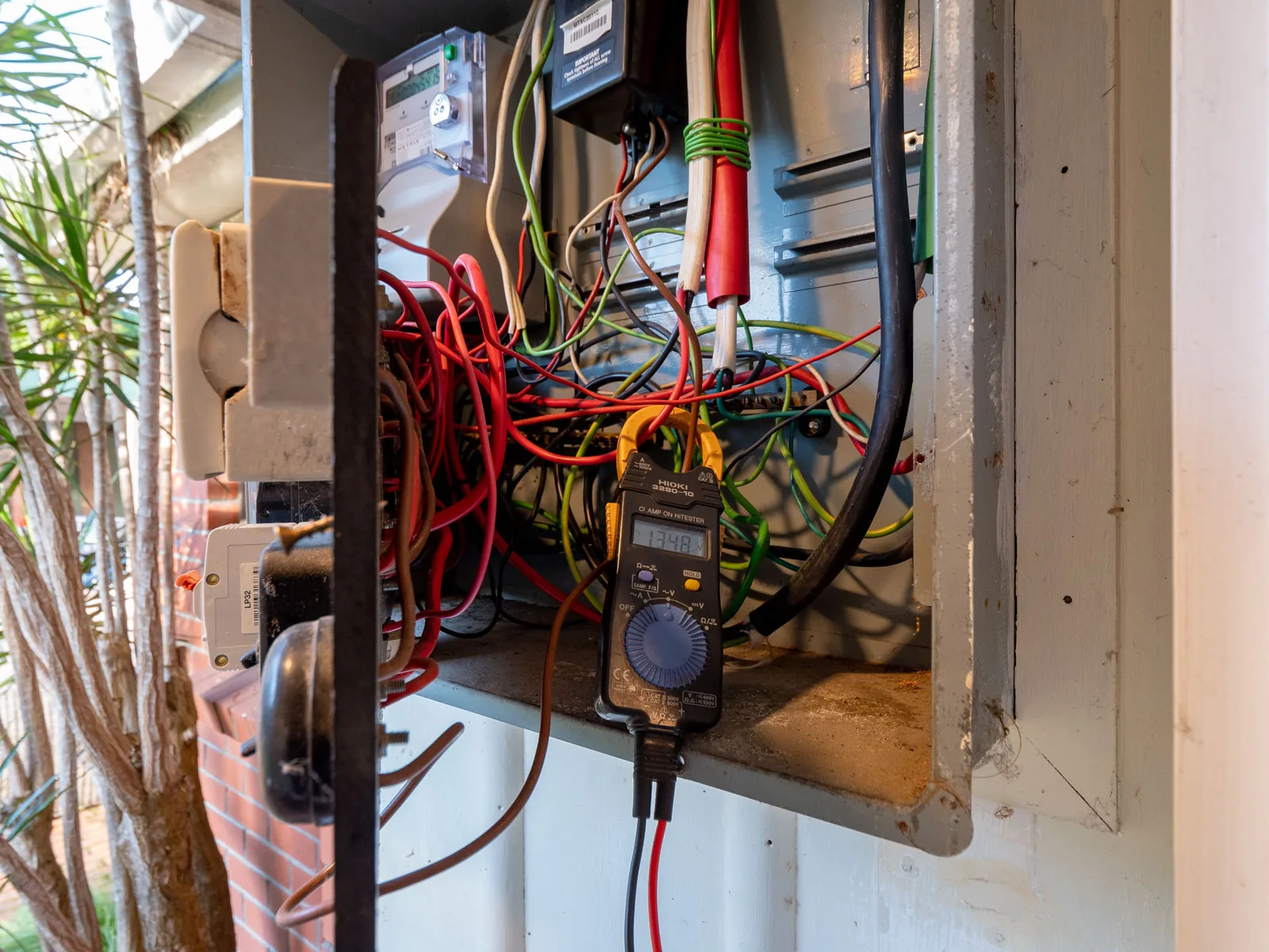 Clamp meter testing an old outdoor meter box on weatherboard