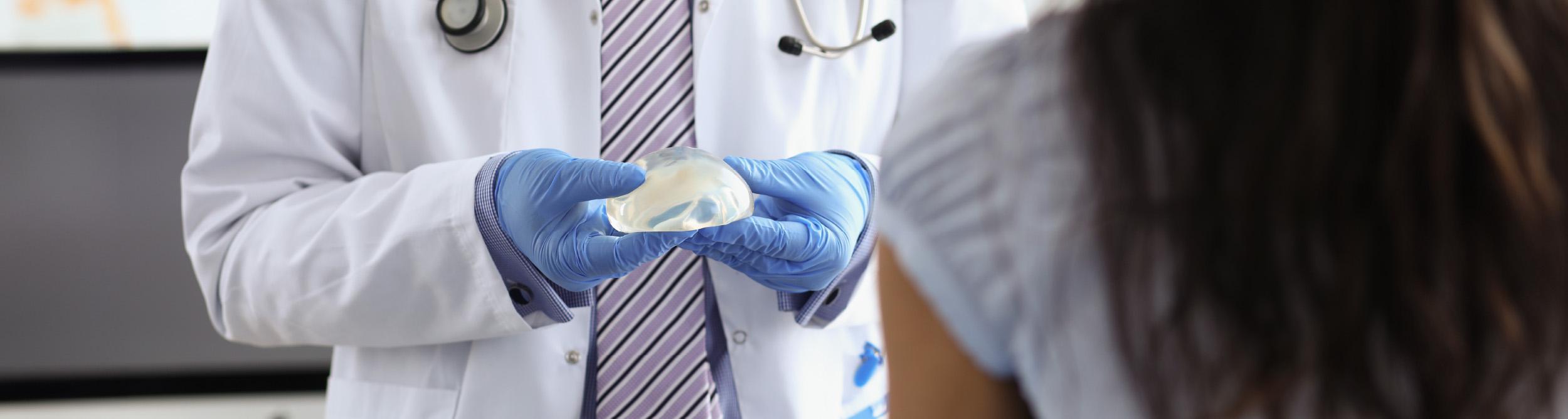 A male patient lying shirtless on a treatment bed wearing a disposable hair net, while a medical professional in a white lab coat and blue latex gloves applies a body sculpting device to his abdomen in a clinical setting.
