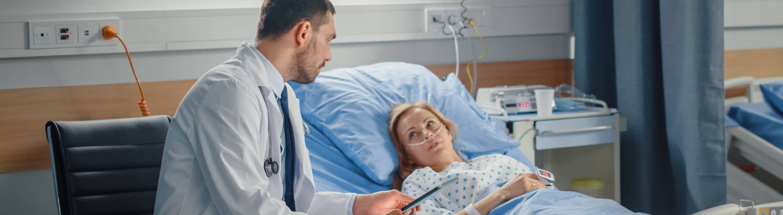 A male patient lying shirtless on a treatment bed wearing a disposable hair net, while a medical professional in a white lab coat and blue latex gloves applies a body sculpting device to his abdomen in a clinical setting.