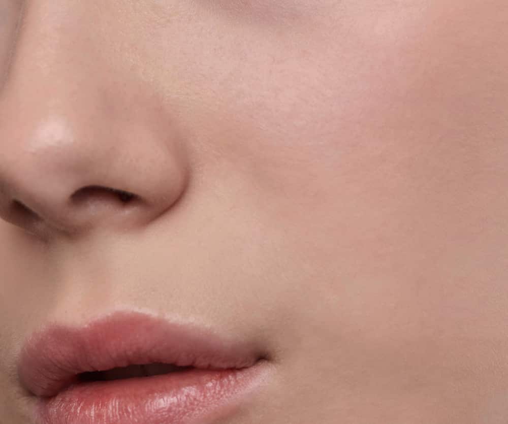 Close-up of a person's nose and lips showing smooth, clear facial skin, used to illustrate a rhinoplasty (nose job) surgery article.