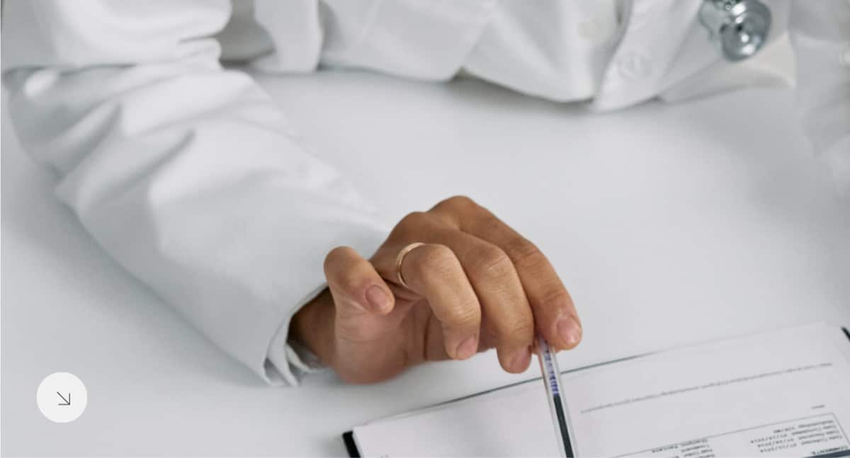 A male patient lying shirtless on a treatment bed wearing a disposable hair net, while a medical professional in a white lab coat and blue latex gloves applies a body sculpting device to his abdomen in a clinical setting.