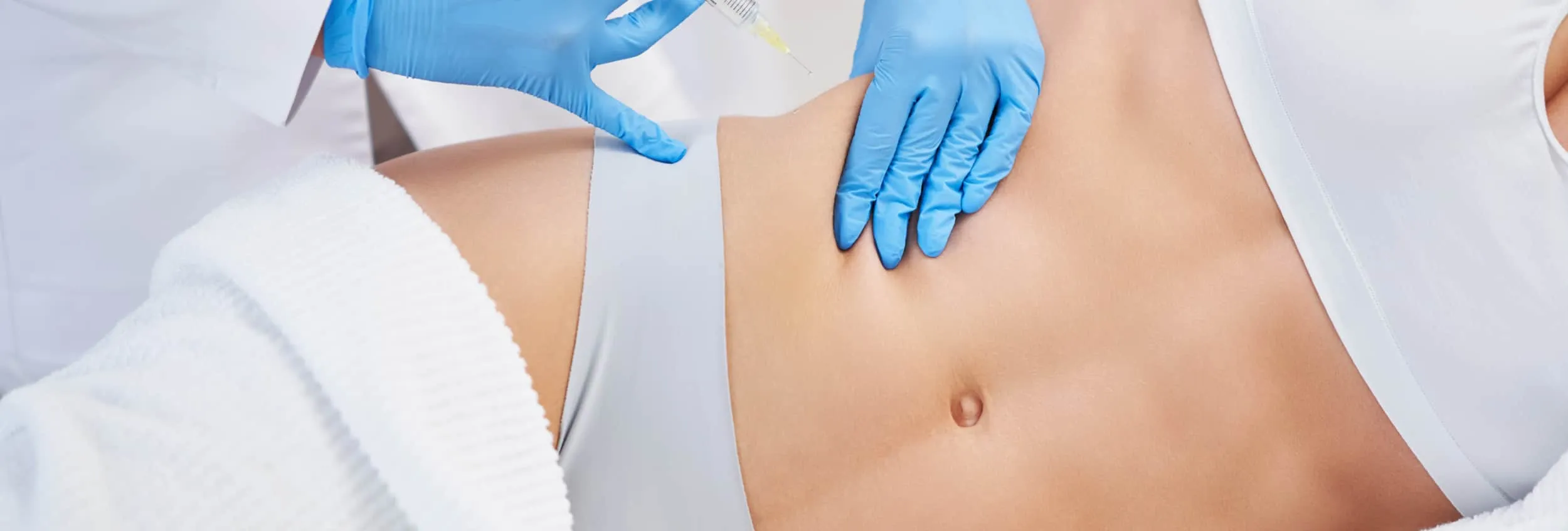 A male patient lying shirtless on a treatment bed wearing a disposable hair net, while a medical professional in a white lab coat and blue latex gloves applies a body sculpting device to his abdomen in a clinical setting.