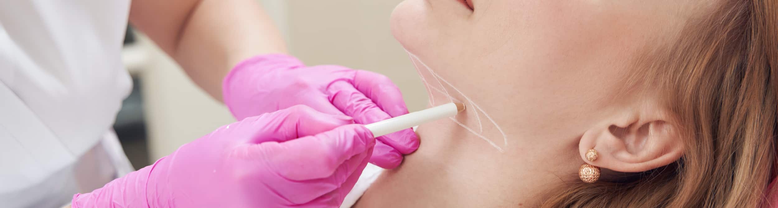 A male patient lying shirtless on a treatment bed wearing a disposable hair net, while a medical professional in a white lab coat and blue latex gloves applies a body sculpting device to his abdomen in a clinical setting.