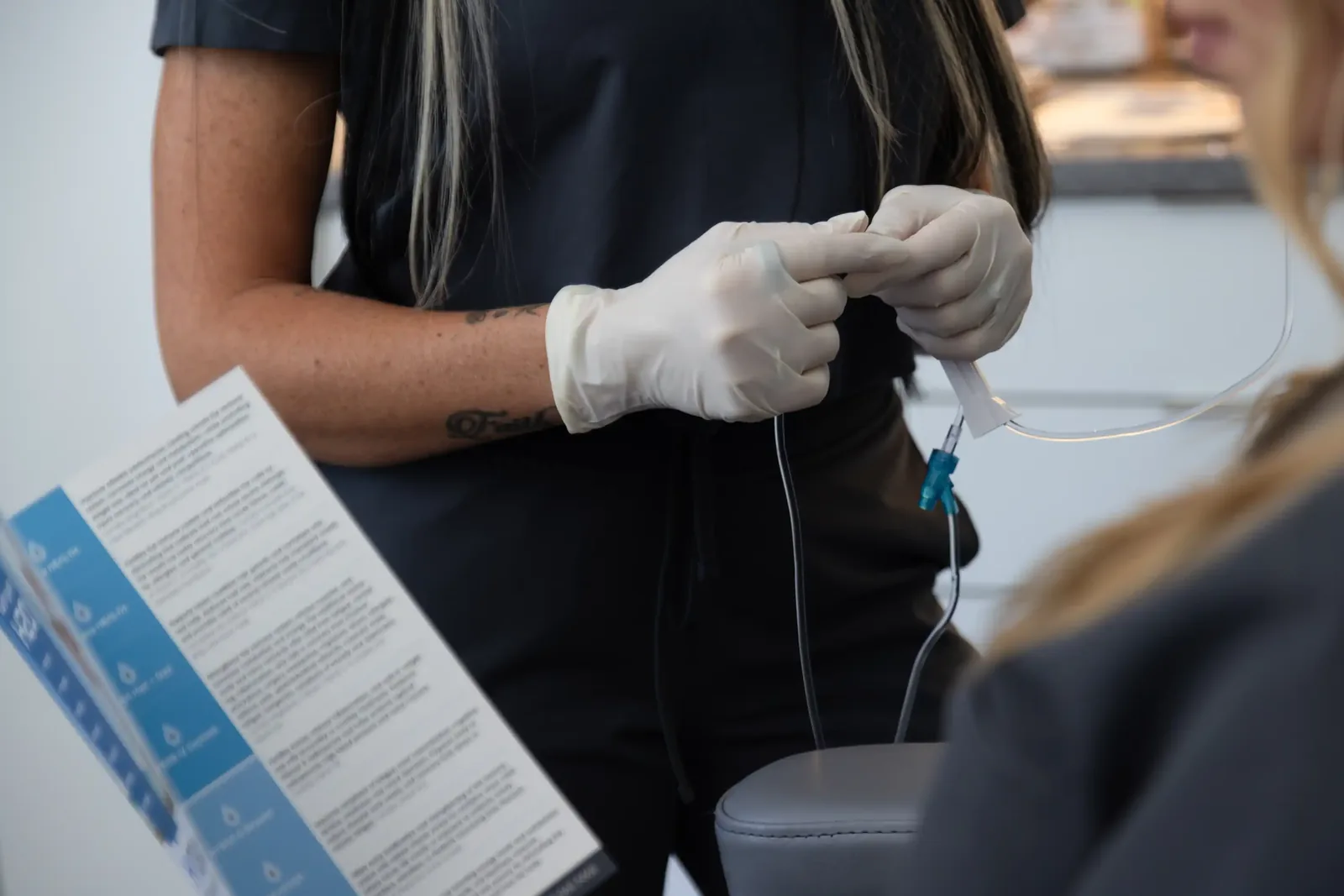 A male patient lying shirtless on a treatment bed wearing a disposable hair net, while a medical professional in a white lab coat and blue latex gloves applies a body sculpting device to his abdomen in a clinical setting.